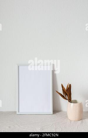 Casa decoratore moccap, quadro vuoto cornice vicino bianco dipinto muro di cemento, rami con foglie asciutte Foto Stock