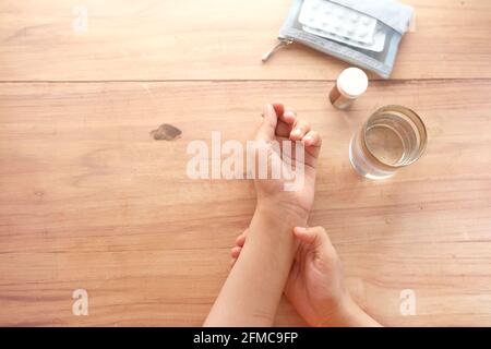 Le mani giovani delle donne che soffrono il dolore del polso con le pillole mediche sopra tabella Foto Stock