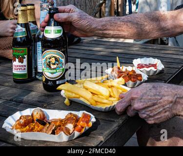 Uno spuntino veloce con currywurst e patatine in una birreria all'aperto presso il Mauer Park, Prenzlauer Berg, Berlino. Mani di anziani Foto Stock