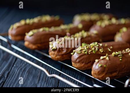 Eclair o profiteroles da dessert francesi con glassa di cioccolato al latte e pistacchi. Torte di pasticceria con panna e condimento. Messa a fuoco selettiva morbida. Foto Stock