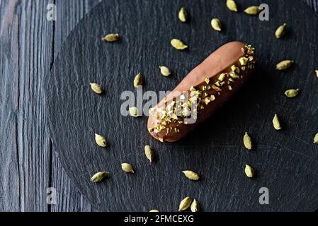 Eclair o profiteroles da dessert francesi con glassa di cioccolato al latte aromatizzata con cardamomo e pistacchi. Torte con crema di pistacchio e condimento. Soft s Foto Stock