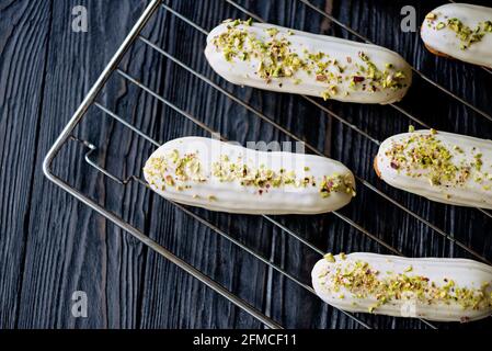 Eclair o profiteroles da dessert francesi con glassa di cioccolato bianco con pistacchi, su una rastrelliera per pasticceria. Torte di pasticceria con crema pasticcera, pistacchio e a. Foto Stock