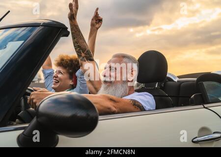 Felice coppia senior che si diverte a guidare su una nuova auto convertibile - persone mature che si divertono insieme durante la vacanza di viaggio su strada Foto Stock