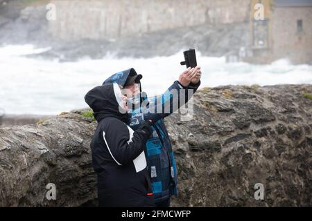 Cornovaglia, Regno Unito. 8 maggio 2021. La gente prende un selfie con il mare ruvido dietro loro malgrado i venti estremamente forti in Porthleven, Cornovaglia. La temperatura era di 12C, la previsione è per pioggia e forti venti nei prossimi giorni. Credit: Keith Larby/Alamy Live News Foto Stock