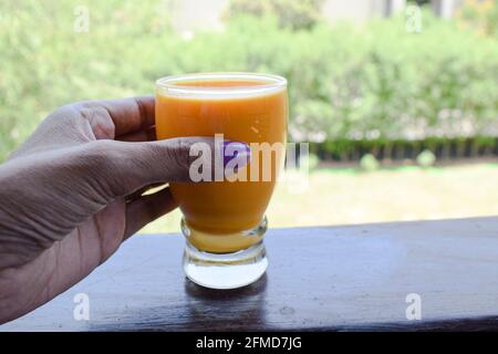 Bicchiere femminile di succo di carote fresco e gustoso preparato mescolando il latte. Succo fatto in casa che beve all'aperto. Succo di carote giamaicano bevanda. Foto Stock