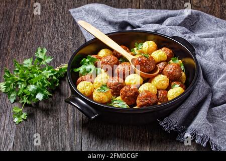 Polpette e palle di spaghetti cotte su un piatto da forno nero - cucina italiana, servita su sfondo di legno scuro con prezzemolo fresco e cucchiaio di legno, Foto Stock
