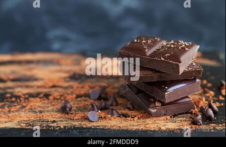 Pila di cioccolato amaro con scaglie di cioccolato, gocce e polvere di cacao su fondo scuro Foto Stock
