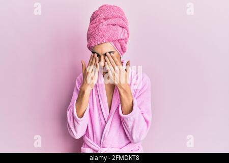 Giovane uomo che indossa donna si compongono portando asciugamano da doccia sulla testa e accappatoio sfregando gli occhi per affaticamento e mal di testa, sonnolenza e espressione stanca. Visione p Foto Stock