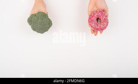 Confronto delle abitudini alimentari. Donna che tiene broccoli e ciambella su sfondo bianco Foto Stock
