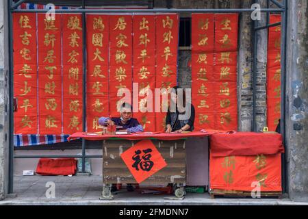 Foshan, provincia di Guangdong, Cina. 8 FEBBRAIO 2021. Un calligrafo sta scrivendo i couplets di festa della molla per la gente. È il cus più comune e importante Foto Stock