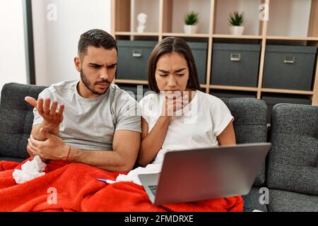 Giovane coppia malata latina che ha teleconsulto medico usando il laptop a casa. Foto Stock