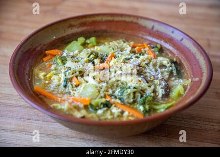 Ciotola fatta in casa con ramen Tom Yum Green Noodle, verdure, curry, goccia d'uovo e un pizzico di parmigiano. Foto Stock