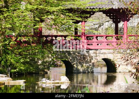 coperto ponte di pietra giapponese con ringhiere di legno rosso nel luce del sole su un fiume Foto Stock