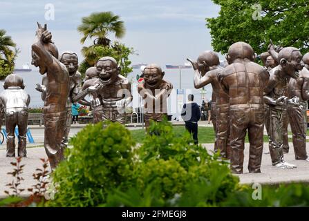 Le statue della scultura A-Maze-ing Laughter dell'artista Yue Minjun si ergono lungo English Bay, dove è ancorato un combattente, a Vancouver, British col Foto Stock