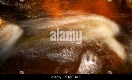 Acqua di colore dorato brillante con bolle sfocate in un ruscello veloce. Foto Stock