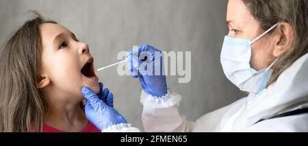 Il bambino apre la bocca per il test PCR COVID-19, il medico tiene un tampone per il campione di saliva della bambina durante la pandemia del virus della corona. Vista panoramica dell'infermiere e. Foto Stock