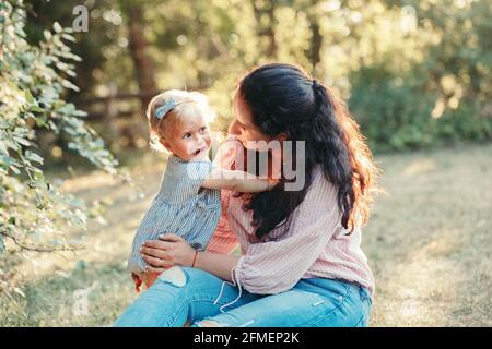 Madre abbracciando pacificante triste sconvolto stressato piangendo bambina. Famiglia mamma giovane e piangendo bambino nel parco all'aperto. Relazione di collegamento di Foto Stock