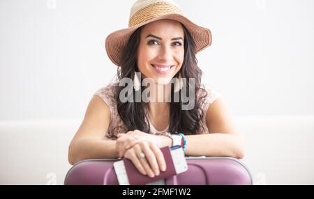 Bella donna viaggiatore pronto per un volo con il suo ticker e passaporto in mani, cappello su, sorriso sul viso e bagagli. Foto Stock