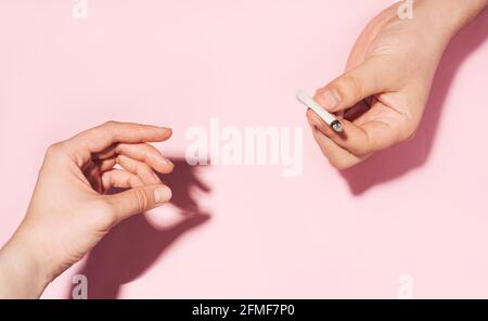 Passare la sigaretta di cannabis di mano in mano. Concetto di fumo di cannabis. Foto color pastello delle mani che si danno a vicenda sigaretta di carta sbriciolante. Foto Stock