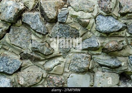 Muro di ciottoli di grandi pietre di granito. Muro di Stome fissato con Malta cementizia. Recinzione o struttura di costruzione in stile vintage Foto Stock