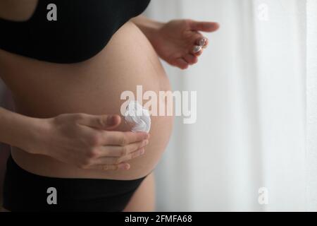 Donne incinte che mettono la crema anti stirata sul suo ventre. Cosmetici per idratare o idratare la pelle in gravidanza. Foto Stock