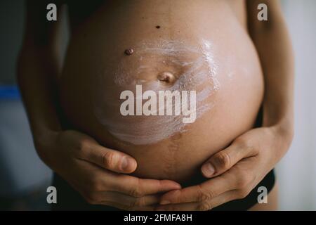 Donne incinte che mettono la crema anti stirata sul suo ventre. Cosmetici per idratare o idratare la pelle in gravidanza. Foto Stock