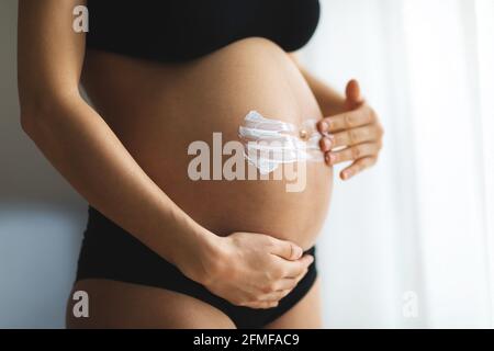 Donne incinte che mettono la crema anti stirata sul suo ventre. Cosmetici per idratare o idratare la pelle in gravidanza. Foto Stock