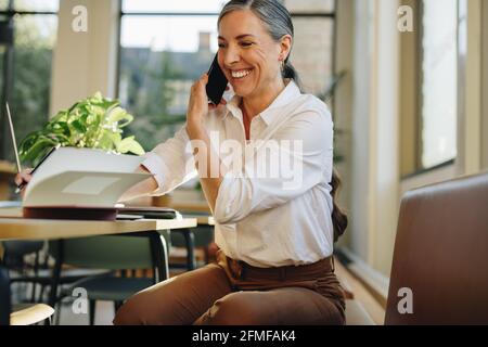 Donna seduta alla scrivania e a scrivere appunti mentre parla al telefono cellulare. donna d'affari che lavora in ufficio e parla al cellulare. Foto Stock