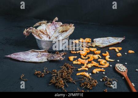 Frutti di mare secchi con calamari secchi e gamberetti secchi su a. tavolo di legno nero Foto Stock
