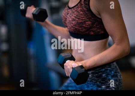 Ragazza con Dumbbells è impegnata nella palestra. Riduce il peso. Cura del corpo. Edificio del corpo. Muscoli forti. Stile di vita sportivo sano. Foto Stock