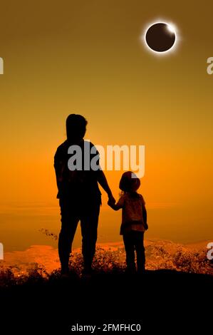 Incredibile fenomeno scientifico naturale. Silhouette vista posteriore di Madre e figlia guardando l'eclissi solare totale che illumina sul cielo arancione in cima alla montagna Foto Stock