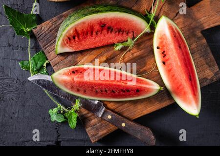 Fette di anguria tagliate a metà su un tagliere di legno. Foto Stock