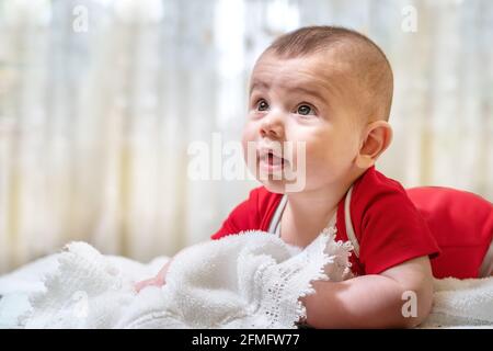 Un neonato sano, un ragazzo di quattro mesi, giace sullo stomaco, riposandosi felicemente. Sullo sfondo della camera da letto. Foto Stock