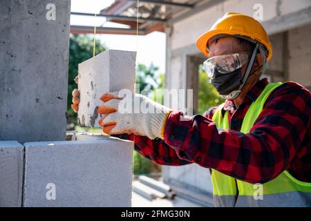 muratore a muratore che lavora con blocchi di calcestruzzo cellulare autoclavati. Walling, installazione di mattoni sul cantiere Foto Stock