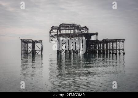 Le tristi rovine del West Pier di Brighton su un insolitamente mare calmo Foto Stock