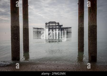 Le tristi rovine del West Pier di Brighton su un insolitamente mare calmo Foto Stock