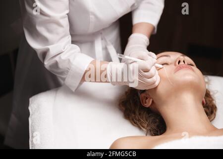 Spa per la cura della pelle e concetto di salone di cosmetologia. La donna riceve il trattamento di cura della pelle in clinica di bellezza, terapista beautician contrassegna le aree a faccia con medico Foto Stock