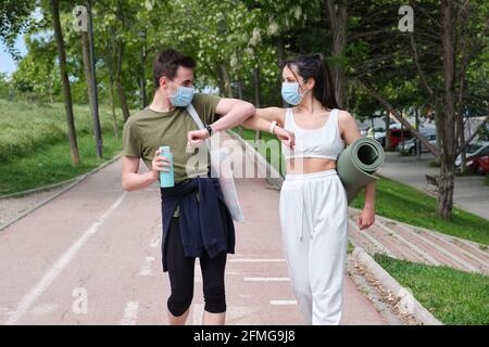 Giovane coppia sportiva con maschere protettive per il viso e saluto con urti a gomiti per prevenire la diffusione del virus corona. Fitness durante i pandemi di coronavirus Foto Stock