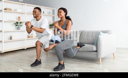 Coppia nera atletica che fa affondi sull'allenamento domestico, spazio di copia. Formazione domestica durante il blocco del covid Foto Stock