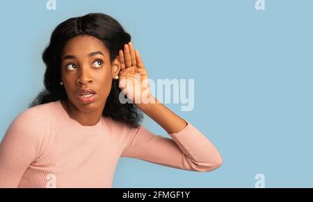 Curiosa giovane femmina nera con la mano vicino all'orecchio che cerca di ascoltare qualcosa Foto Stock