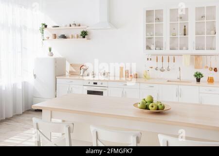 Luminoso interno cucina. Mobili e ripiani bianchi con utensili e piatti, piccolo frigorifero vicino alla finestra Foto Stock