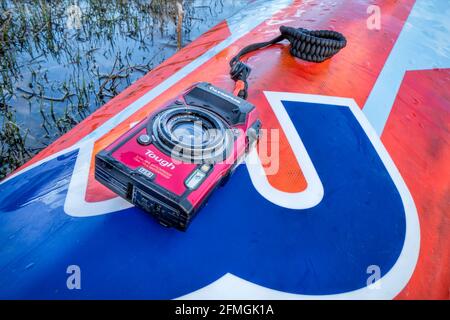 Fort Collins, CO, Stati Uniti d'America - 4 maggio 2021: Compatta, impermeabile Olympus Stylus Tough TG-5 fotocamera su un ponte bagnato di un stand up paddleboard di Mistral Foto Stock