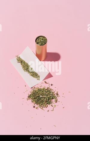 Foto hipster di lattina, carta e foglie di Cannabis secco su sfondo rosa con forme dure, layout. Foto Stock