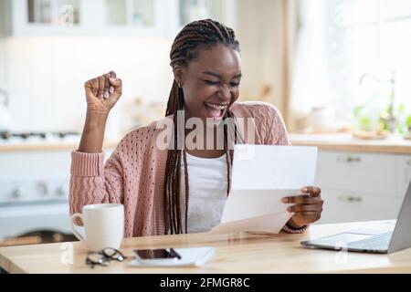 Buone notizie. Ritratto della lettera di lettura della Signora Africana americana overjoyed in cucina Foto Stock