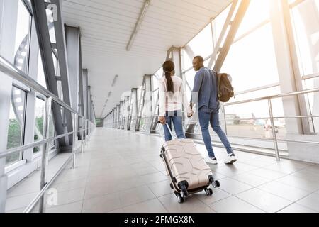 Viaggiare insieme. Romantica coppia afroamericana con bagaglio a piedi nel terminal dell'aeroporto Foto Stock