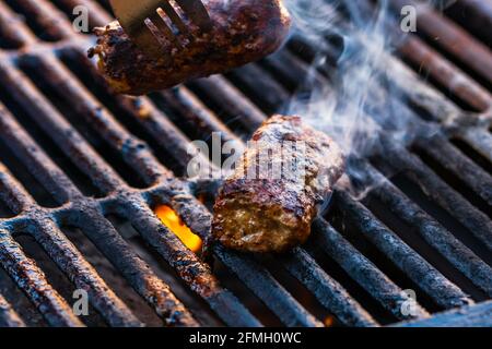 Un closeup di involtini di carne chiamato mici o mitigei su barbecue con fumo crescente Foto Stock