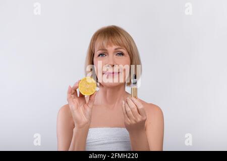 Acidi di frutta per il concetto di cura della pelle. Bella donna matura che tiene limone e siero ringiovanente su sfondo studio chiaro Foto Stock