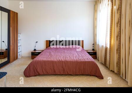 Accogliente camera da letto interna con ampio letto matrimoniale coperto di copriletto rosa. Foto Stock