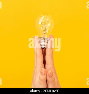 Concetto della nuova idea, lampadina in mano primo piano su sfondo giallo arancio, foto isolata Foto Stock