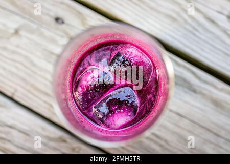 Vista dall'alto in piano di vetro di rosso porpora scuro succo di barbabietola con ghiaccio isolato con sfondo sfocato di legno piano della terrazza Foto Stock